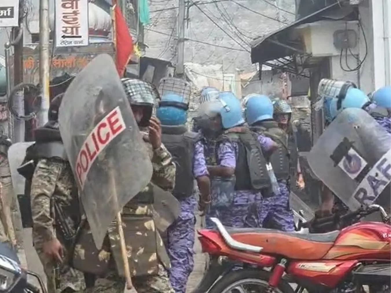 पुलिस और आरएएफ के जवान दंगा रोधी गियर में एक शहरी गली में खड़े हैं।