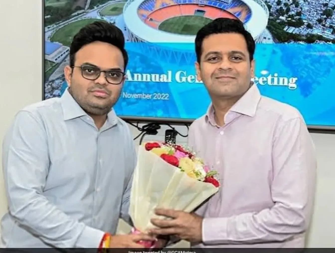 दो आदमी एक गुलदस्ता पकड़े हुए हैं, एक आदमी चश्मा पहने हुए है।