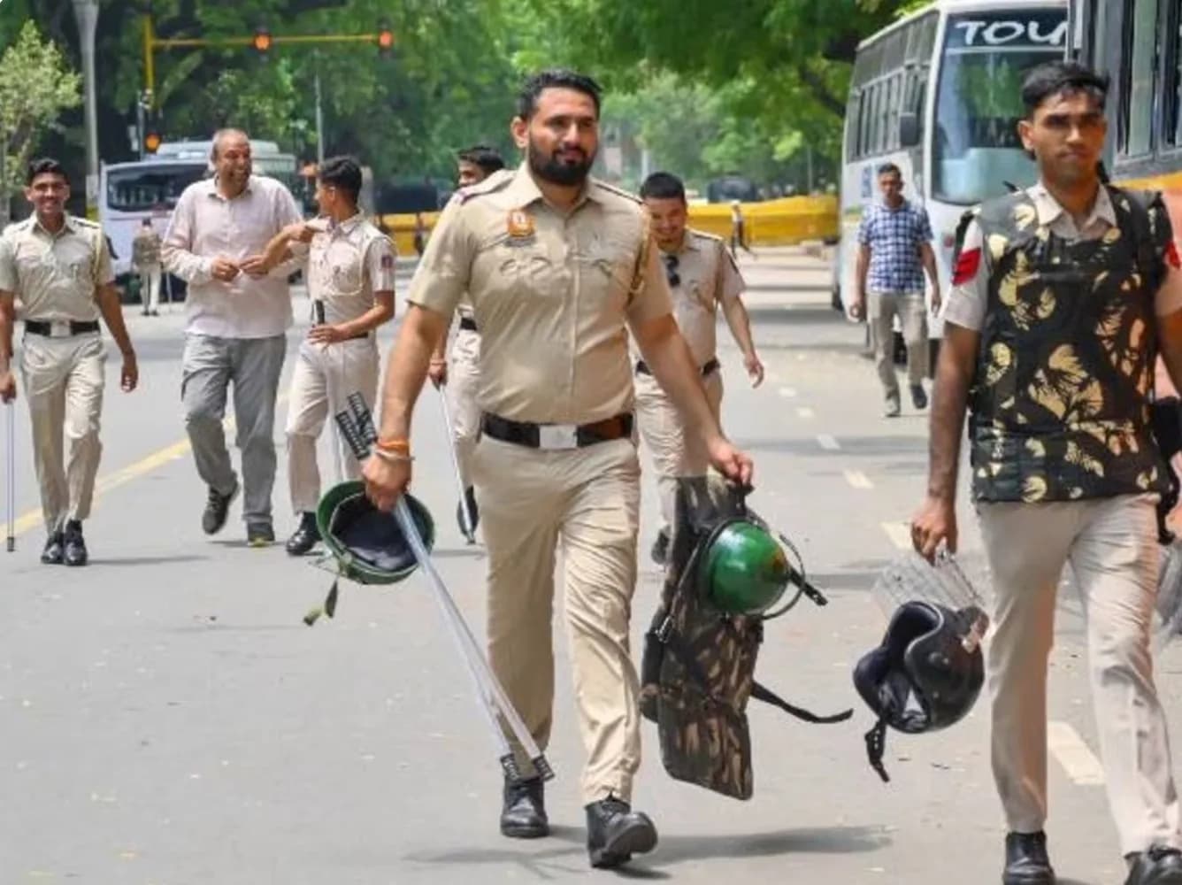 पुलिसकर्मी लाठी, ढाल और हेलमेट लेकर सड़क पर चल रहे हैं।
