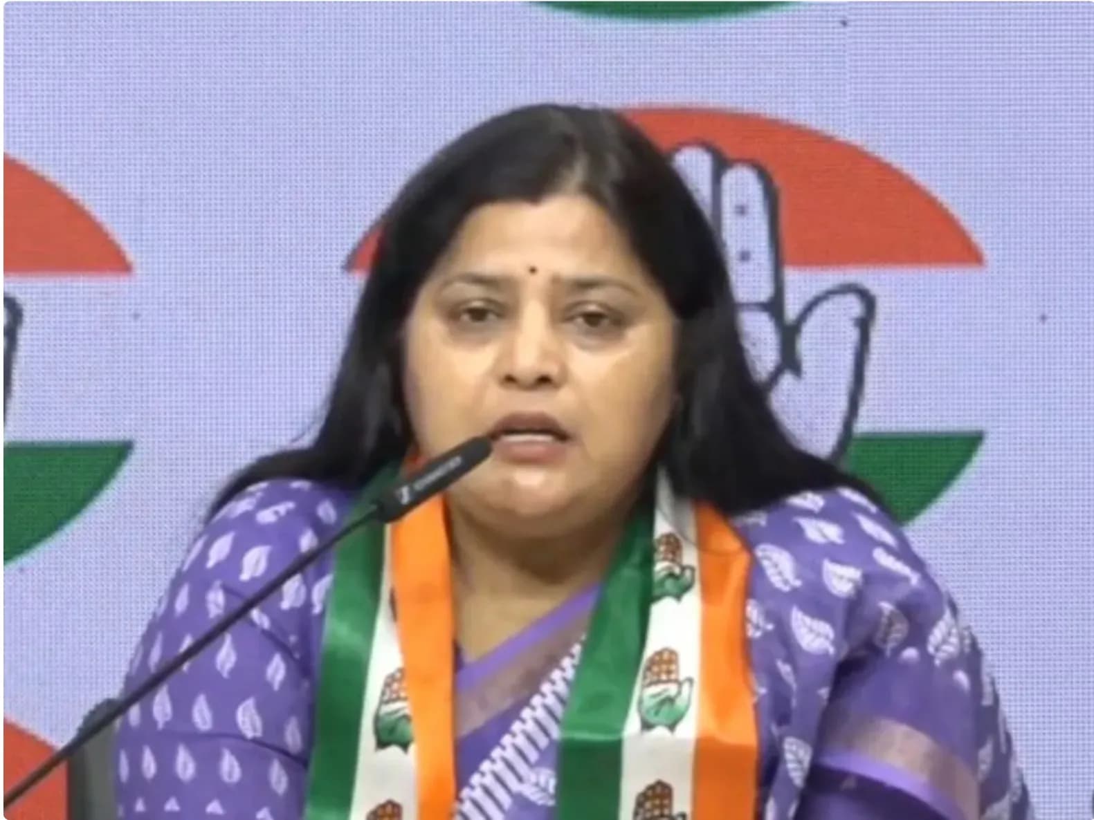 एक महिला कांग्रेस पार्टी के झंडे के साथ बोल रही है।