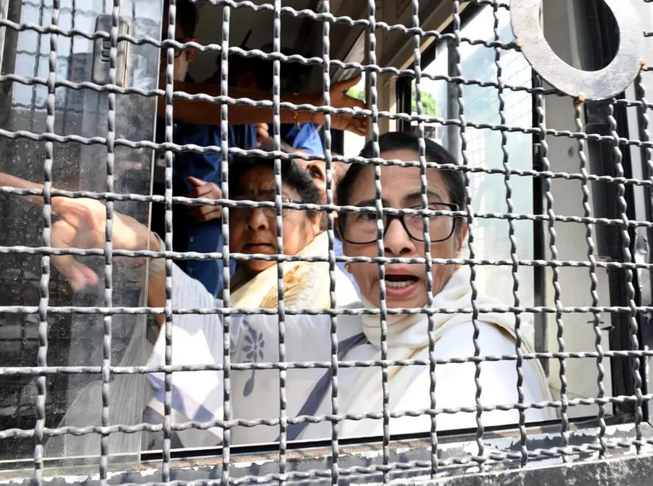 दो महिलाएँ लोहे की सलाखों के पीछे से बाहर देख रही हैं।