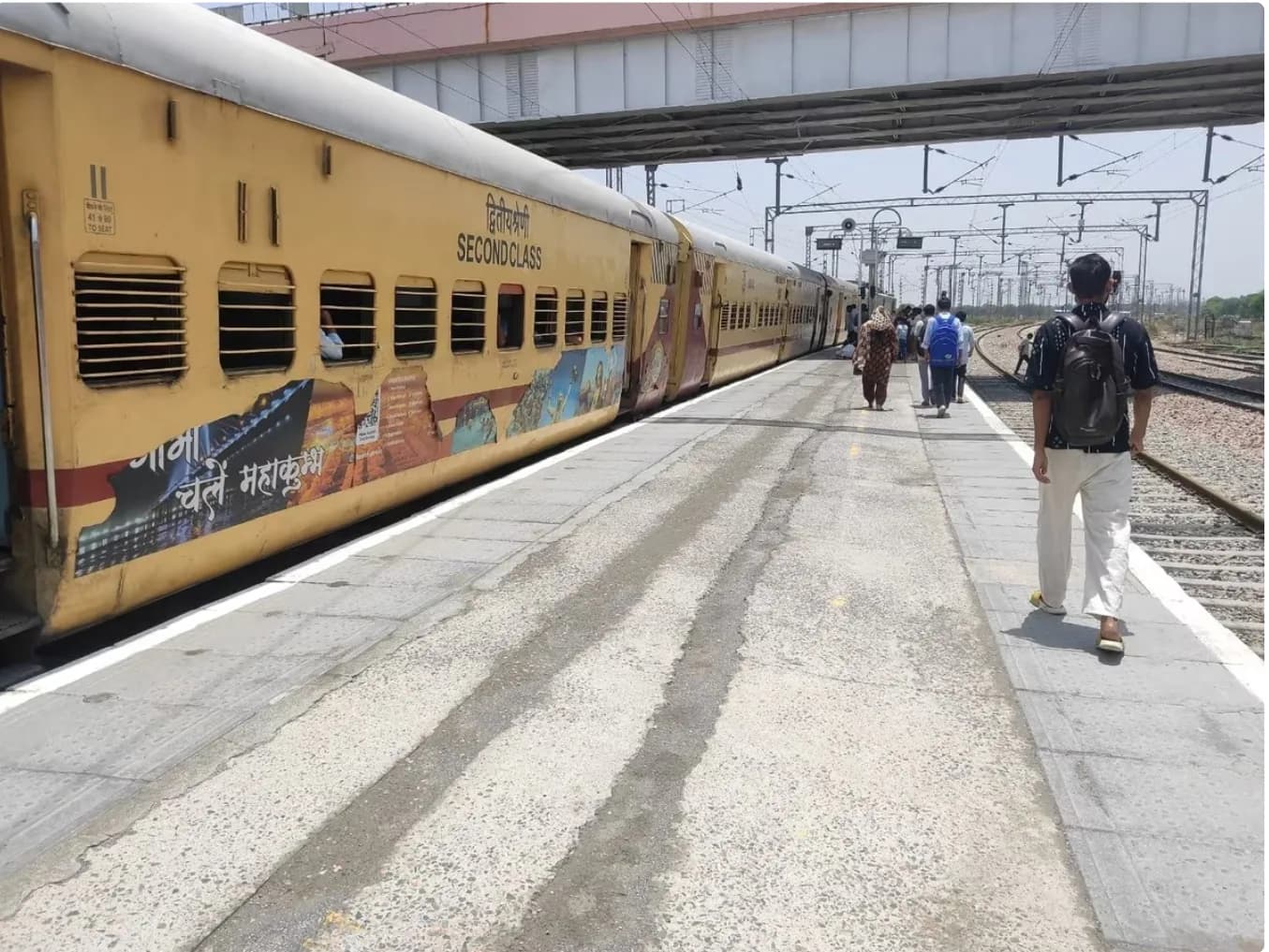 एक पीली ट्रेन प्लेटफॉर्म पर खड़ी है और लोग उस पर चढ़ रहे हैं।