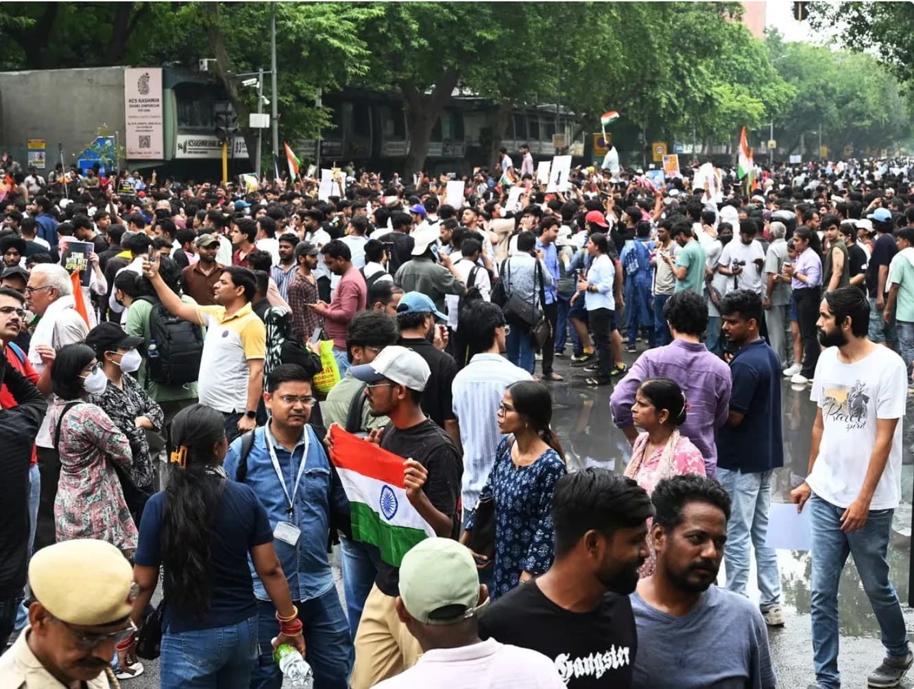सड़क पर बड़ी संख्या में लोग विरोध प्रदर्शन कर रहे हैं, कुछ ने भारतीय झंडे पकड़े हुए हैं।