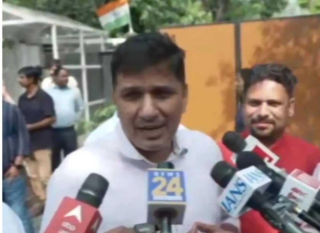 एक आदमी पत्रकारों को संबोधित कर रहा है, जिसके पीछे भारतीय झंडा है।