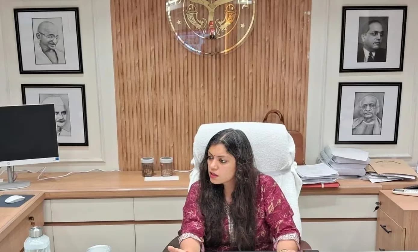 एक महिला अपने कार्यालय में बैठी है जिसके पीछे नेताओं की तस्वीरें लगी हैं।