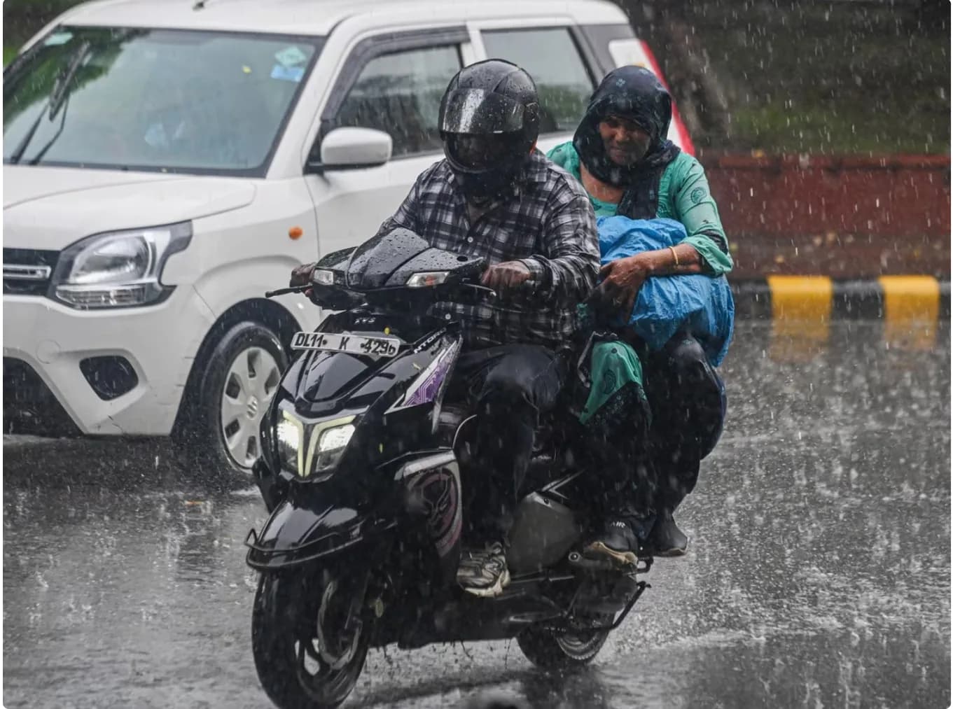 बारिश में एक स्कूटर पर सवार एक आदमी और एक महिला सड़क पर जा रहे हैं।