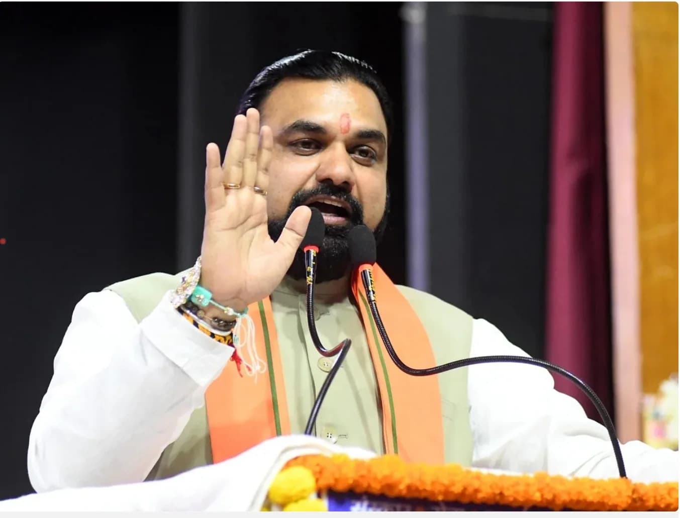 एक व्यक्ति मंच पर भाषण दे रहा है और अपना हाथ उठा रहा है।